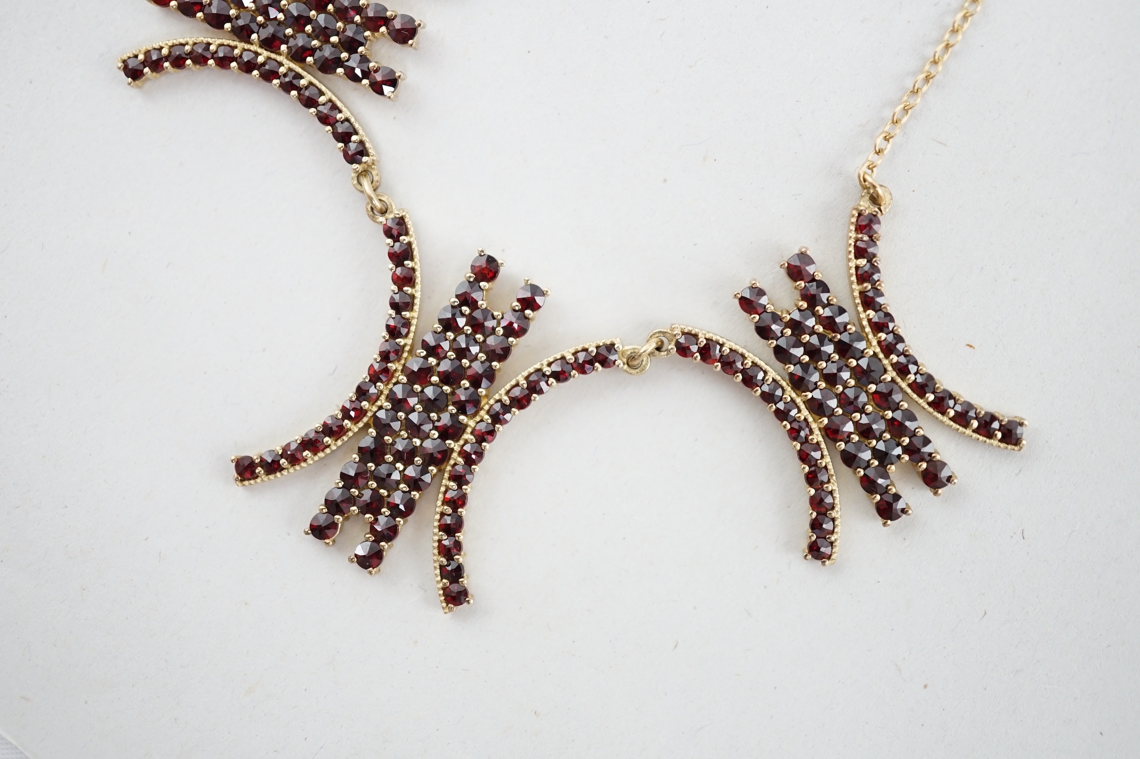 A yellow metal and garnet cluster set fringe necklace, with three stylised motifs, 45cm, gross weight 15.2 grams. Condition - fair to good